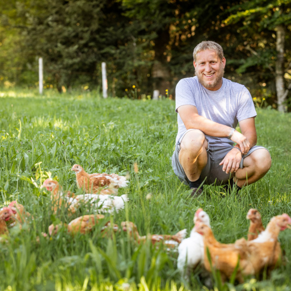 Norbert Schedler hockt zusammen mit seinen Ländle Wiesenhühnern auf der Wiese | Foto: Weissengruber & Partner