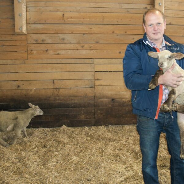 Bernd Bechter steht in einem Stall und hat ein Lamm auf dem Arm