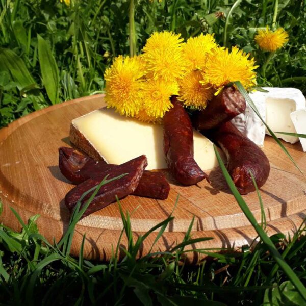 Käse und Wurstprodukte sind schön auf einem Holzteller präsentiert, welcher auf einer Blumenwiese steht