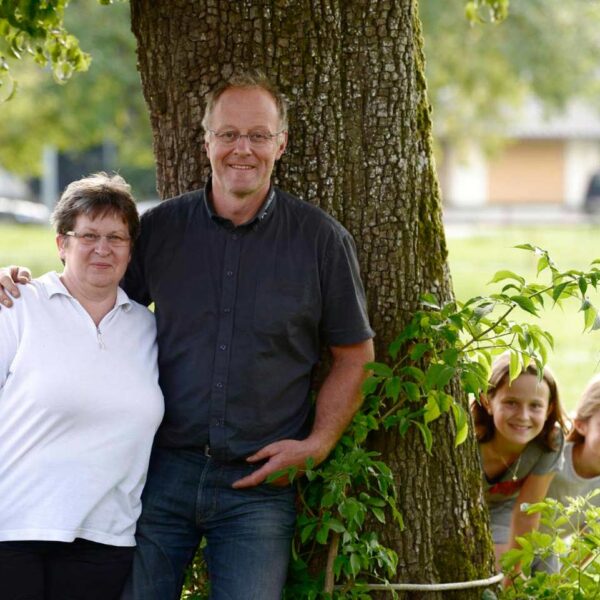Albert Büchele steht mit seiner Frau im Arm vor einem Baum, während zwei Kinder hinter dem Baum hervorschauen
