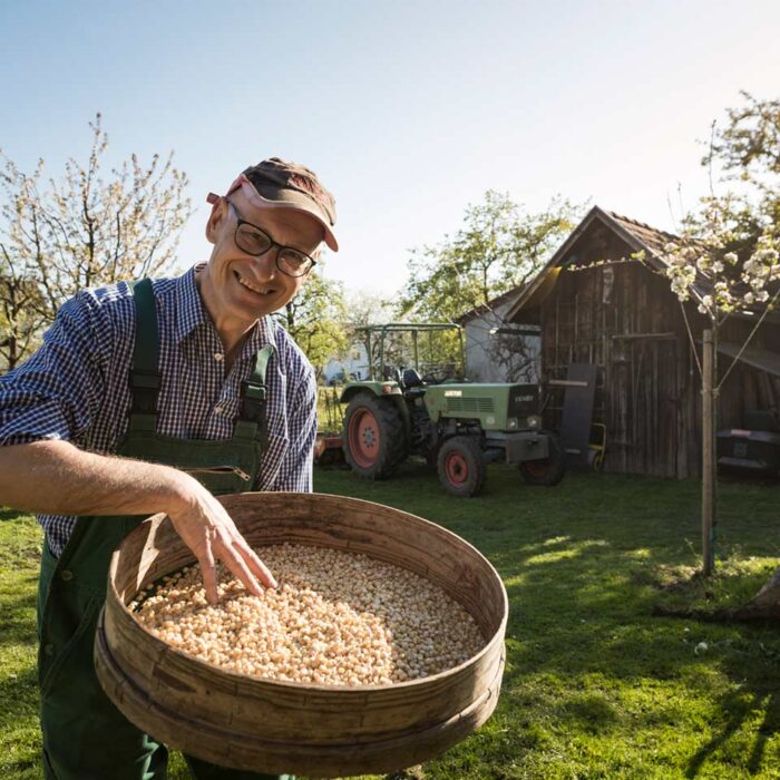 Richard Dietrich steht in seinem Garten und hält ein Sieb mit getrockneten Riebelmaiskörnern in der Hand.