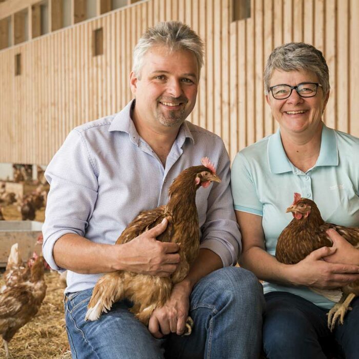 Claudia und Gerd Giselbrecht sitzen in ihrem Hünherstall inmitten der Hühner. Beide halten ein Huhn in der Hand.