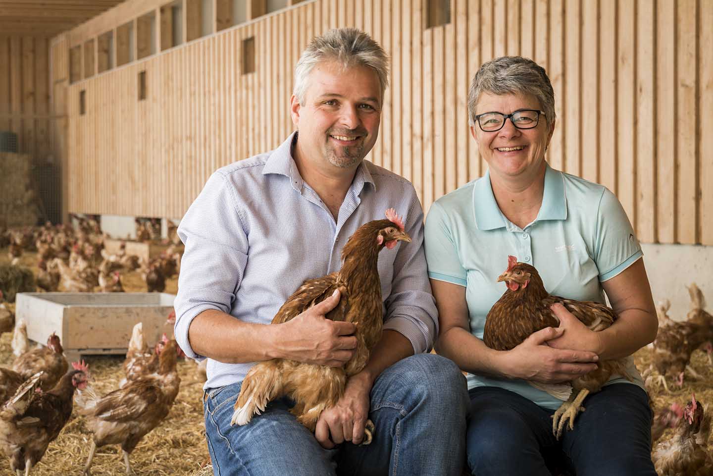 Claudia Und Gerd Giselbrecht Sitzen In Ihrem Hünherstall Inmitten Der Hühner. Beide Halten Ein Huhn In Der Hand.
