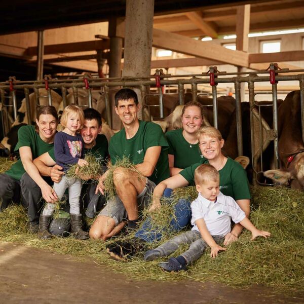 Die zwei Brüder Mathias und Andreas sitzen mit ihren Familien im Stall vor den Kühen im Heu.