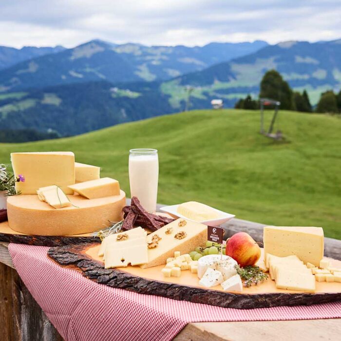 Alpe Gemeine Brongen - Milchprodukte der Alpe auf einem Brett vor Bergpanorama - Foto: Pallinger