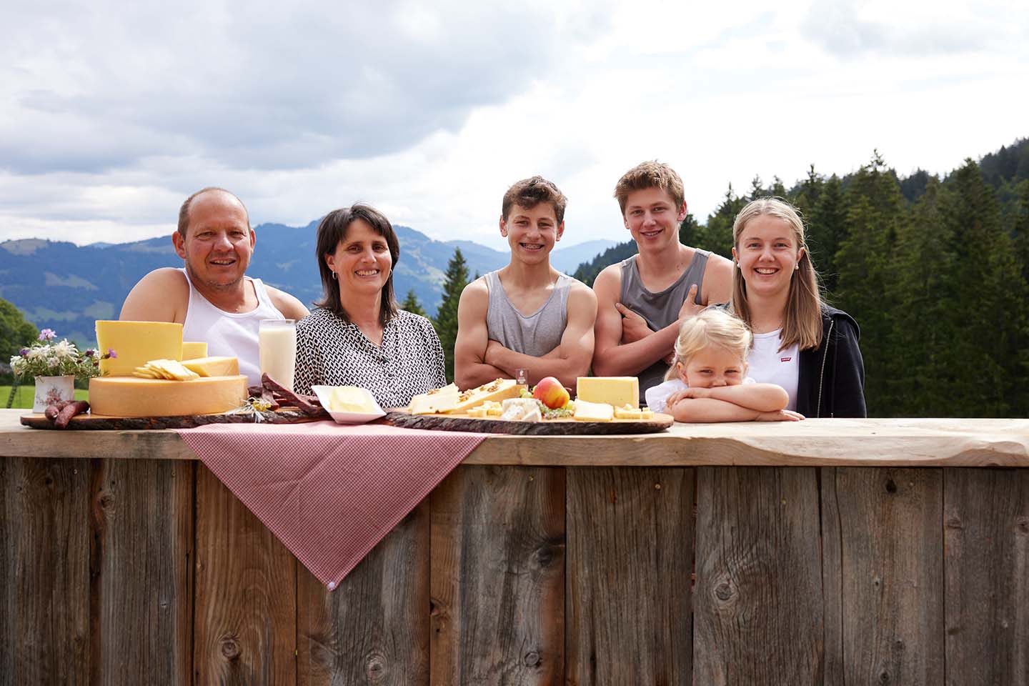 Die Familie Meusburger Steht Hinter Einer Holzbar Auf Der Herhafte Käseplatten Der Alpe Gemeine Brongen Aufgetischt Sind.