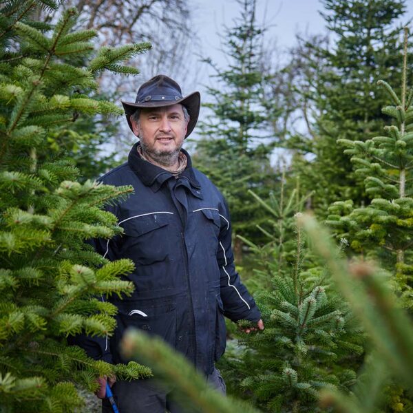 Peter Fink steht mit Cowboy-Hut inmitten seiner Christbaumkultur und lächelt in die Kamera.