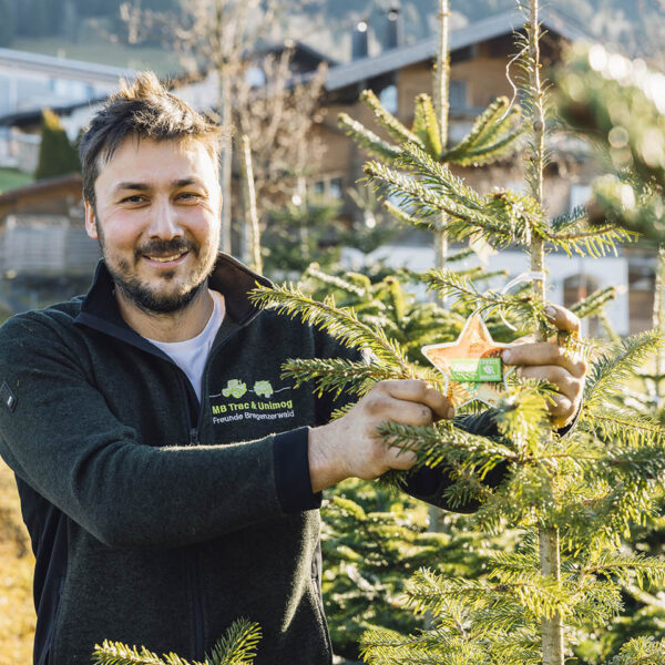 Gmeiner Laurin steht neben neben einen Ländle Christbaum und hält den Stern mit Gütesiegel in die Kamera.
