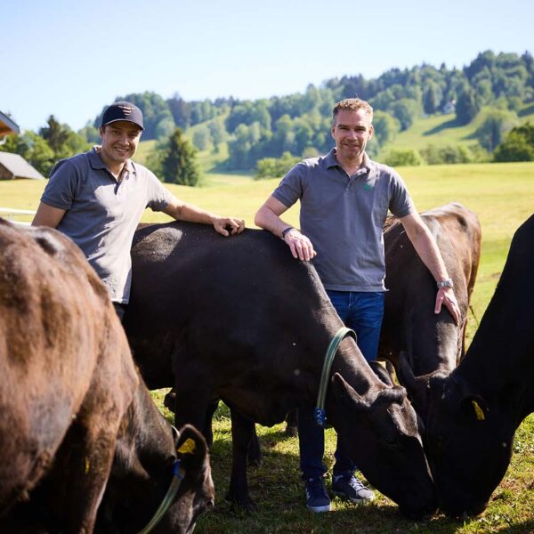 Wolfgang Rigo und Betriebsleiter Christoph Burtscher stehen zwischen den Rindern auf der Weide vor dem Petrlehof.